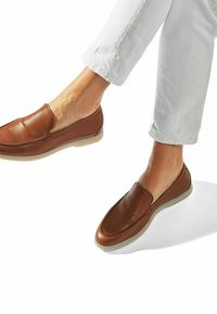 Brązowe skórzane buty typu slip-on z detalami szycia, gładką powierzchnią i lekką gumową podeszwą, w połączeniu z białymi, zwiniętymi spodniami.