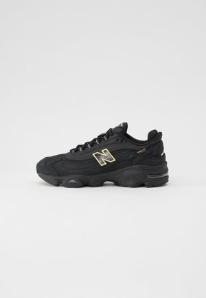 Zapatilla negra con parte superior texturizada, sistema de cordones prominente y suela de goma. Presenta un logotipo en contraste y acentos laterales.