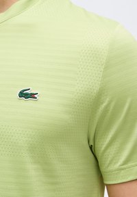 Ανοιχτό πράσινο πικέ πόλο με κοντά μανίκια και μικρό πράσινο λογότυπο κροκόδειλου στο αριστερό μέρος του στήθους.