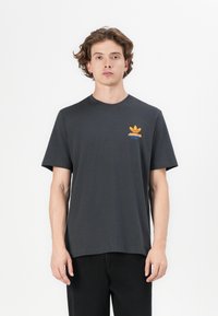Fekete pamut póló rövid ujjakkal, kerek nyakkivágással és narancssárga Adidas logóval a bal mellen. Egyszerű szabás, minta nélkül.