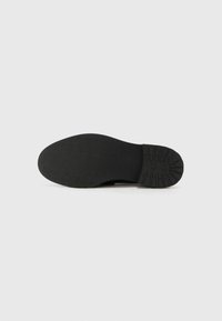 Black shoe sole with a smooth flat surface and patterned tread design, featuring a rounded toe and subtle branding near the heel.
