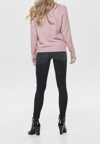 Jasno różowy sweter z prążkowanymi mankietami i dołem; w zestawie z dopasowanymi ciemnoszarymi dżinsami. Czarne botki na obcasie z rękawem z zamkiem.