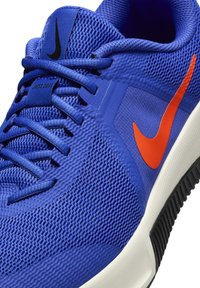 Blue mesh athletic shoe with textured upper, contrasting orange swoosh, black accents, and white midsole, featuring traditional lacing system.