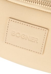 Beżowy materiałowy woreczek z skórzaną metką z napisem "BOGNER." Wyposażony w zamek błyskawiczny i gładką teksturę.