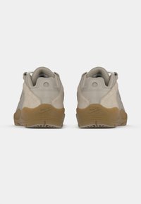 Αθλητικά παπούτσια Nike σε γκρι σουέντ και δίχτυ, με σόλα από καουτσούκ σε καφέ απόχρωση, στρογγυλεμένο πίσω μέρος και ελάχιστα διακριτικά σημάδια. Εμφανίζεται από πίσω όψη.