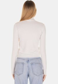 Maglione aderente color crema con texture a coste, maniche lunghe e collo alto, abbinato a jeans azzurri leggermente consumati.