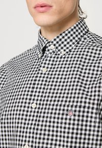 Sort-hvidt gingham ternet skjorte med knap-ned krave, der har et lille broderet logo på brystlommen og hvide knapper.