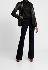 Svart läderblazer över en åtsittande svart topp, i kombination med mörkblå utsvängda jeans. Påtagliga texturer och former genom hela outfiten.