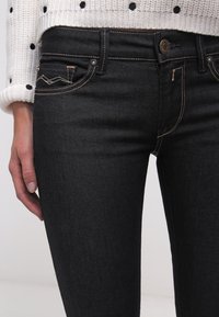 Jeans de mezclilla oscura con una forma ajustada, costuras claras y un diseño sutil en los bolsillos. Combinados con un suéter de punto con lunares.