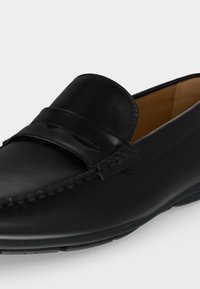 Mocassin en cuir noir avec surpiqûres mocassin et détail de bride penny, avec un intérieur marron clair et une semelle en caoutchouc pour le confort et l'adhérence.