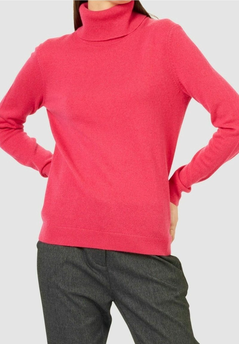 Pull fuchsia avec un col roulé haut et des manches longues, fabriqué en tissu doux. Associé à un pantalon gris, la tenue présente une texture lisse.