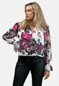 Kwiatowa bluzka w kolorze białym z różowymi, fioletowymi i zielonymi wzorami; ma długie rękawy z falbanami oraz dekolt w kształcie litery V. Nosi się z czarnymi spodniami.