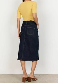 Gonna midi in denim scuro con taglio dritto, dotata di tasche sul retro e impunture gialle a contrasto. Abbinata a un top giallo a coste e tacchi.