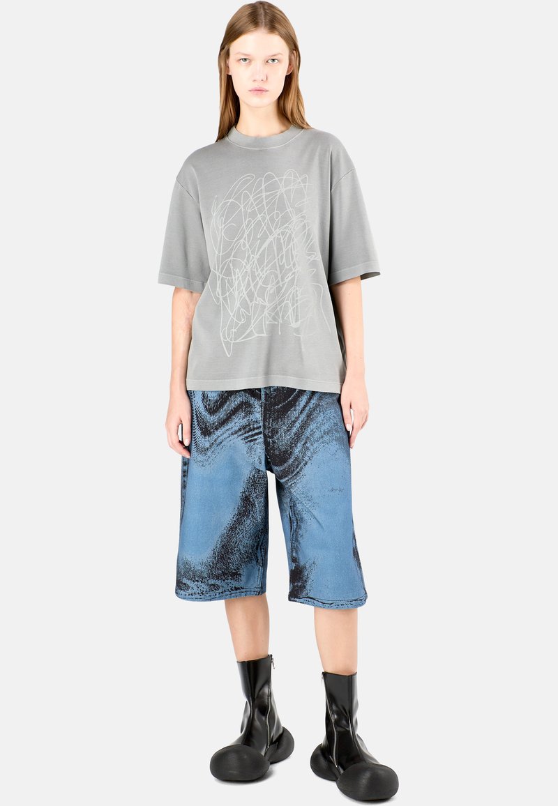 Grey oversized t-shirt with abstract white pattern, paired with blue denim shorts featuring black textured accents and black ankle boots.
