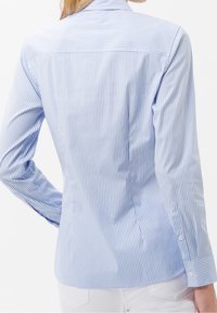Chemise rayée bleue et blanche au design ajusté, manches longues, ourlet incurvé et détails en boutons sur les poignets. Tissu en coton lisse.