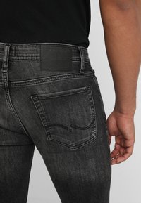 Jeans de mezclilla negros con un diseño ajustado, con un parche de cuero y costuras sutiles en los bolsillos traseros. Lleva en la cintura.
