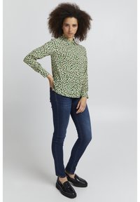 Camicia verde con motivo leopardato, maniche lunghe e colletto, abbinata a jeans skinny scuri e mocassini neri.