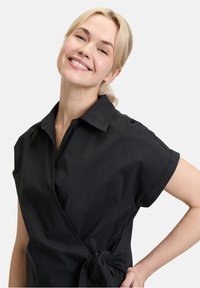 Schwarzes, kurzärmeliges Wickelkleid mit kragenähnlichem Ausschnitt und seitlichem Bindedetail. Glattes Material, taillierte Passform und minimalistisches Design.