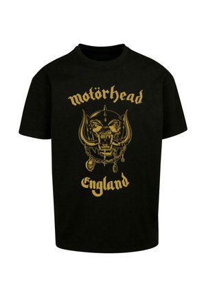 Melnā kokvilnas T-kreklā ir zelta grafiskais dizains ar skeletu ar ragiem un tekstu "motörhead" un "Anglija" zem tā.