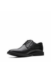 Zapato de vestir negro de cuero con cierre de cordones, punta redondeada, textura lisa y suela de goma baja. Diseño minimalista con costuras sutiles.