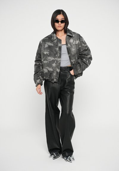 Grijze camouflage bomberjack, grijze tanktop en zwarte leren wide-leg broeken, gecombineerd met zilveren puntige schoenen.