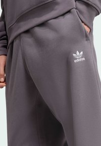 Sive poliester hlače za trening s opuštenim krojem, s bočnim džepovima i malim bijelim Adidas logotipom s lijeve strane. Mekani materijal.