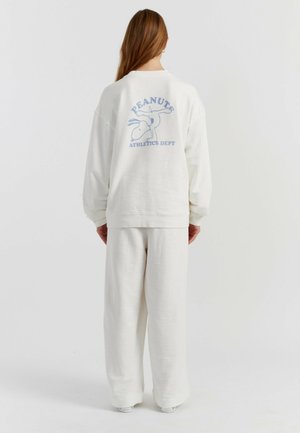 Sweat-shirt blanc surdimensionné avec un graphisme bleu clair indiquant "PEANUTS ATHLETICS DEPT" au dos, accompagné d'un pantalon ample assorti.