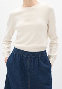 Gräddfärgad stickad tröja med rund halsringning tillsammans med en denimkjol med elastisk midja och sidofickor.