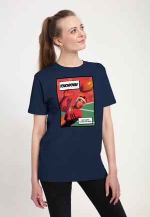 Ung kvinde iført mørkeblå t-shirt med tegneseriestil af en amerikansk fodboldspiller, der griber bolden, og teksten "TOUCHDOWN! Han har scoret for at vinde kampen."