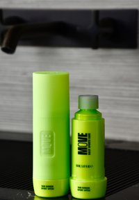 Deux contenants de crème solaire verts néon : un tube cylindrique strié et une bouteille plus courte avec un bouchon à vis, tous deux étiquetés "MOVE" et SPF 30.