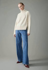 Pull à col roulé en tricot crème avec des poignets côtelés, associé à un jean large bleu clair et des talons aiguilles bordeaux.