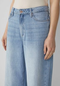 Hellblaue Denim-Jeans mit weitem Bein und hoher Taille, ausgestattet mit Gürtelschlaufen, einem Knopfverschluss und subtilen Verwaschungen am Stoff.