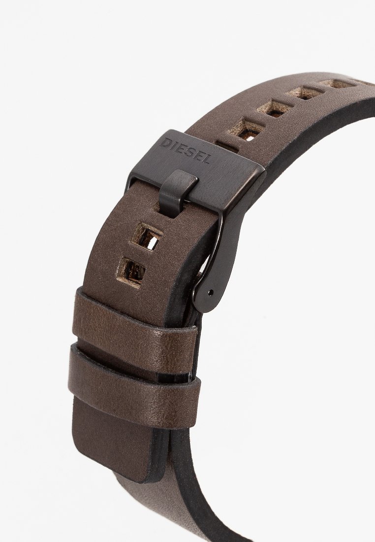 Correa de reloj de cuero marrón con diseño perforado y hebilla de metal negro. Presenta una marca grabada en la hebilla y dos correas de cuero ajustables.