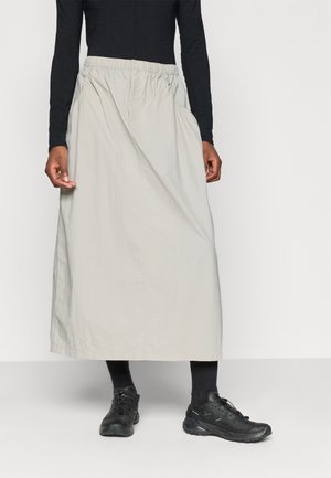 Jupe longueur cheville gris clair avec une taille élastique, poches latérales et un tissu léger et lisse. Portée avec des chaussures de sports noires.