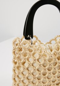 Sac à main en perles avec une base en tissu crème, un motif tissé complexe et une poignée noire brillante. Comprend un détail d'anneau en métal argenté.