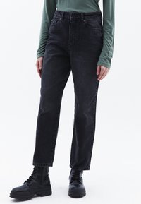 Jeans negros de tiro alto, hechos de denim, con un diseño de pierna recta y estilo de cinco bolsillos. Combinados con botas negras de cordones.