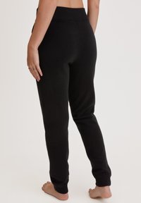 Zwarte, zachte loungebroeken met een geribbelde tailleband en boorden. Getailleerde pasvorm, minimale details, te zien vanuit de achterkant.