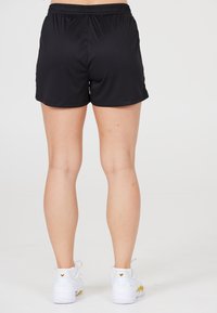 Sorte atletiske shorts med elastisk talje, glat tekstur og længde til midt på låret, parret med hvide sneakers med gule detaljer.