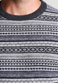 Pull en tricot présentant un motif à rayures gris et marine avec diverses textures et motifs géométriques, col côtelé et tissu doux.