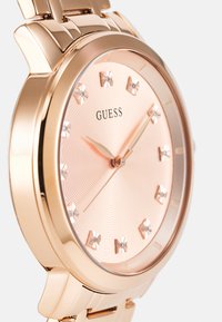 Montre en or rose avec un cadran rond, dotée d'un cadran rose texturé, d'index horaires en or rose et d'un bracelet en métal lisse.