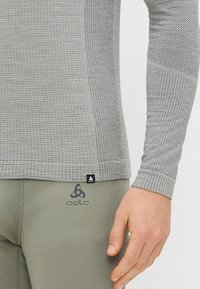 Couche de base à manches longues grise avec un motif texturé ; présente un design ajusté et un col rond. Logo Odlo affiché sur le torse et la taille.