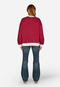 Bordó pulcsi kerek nyakkivágással és fehér díszítéssel, laza szabással és bordás mandzsettával, trapéz farmernadrággal párosítva.