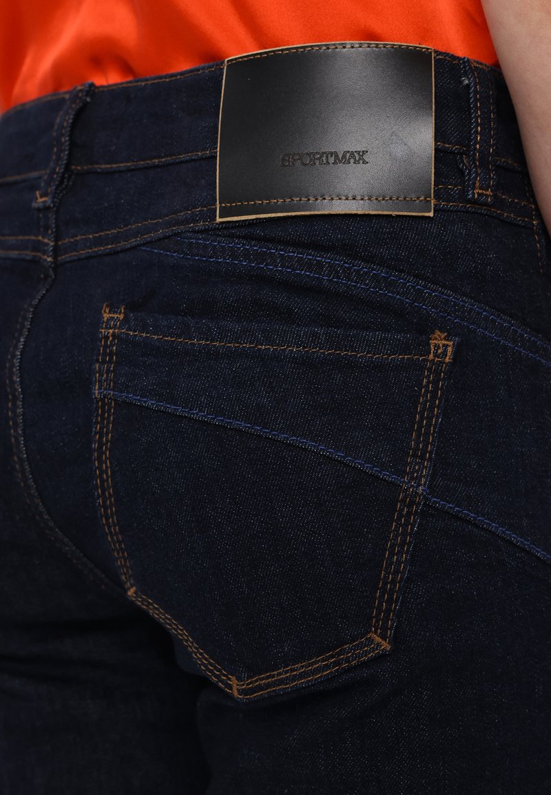Dark denim jeans with a fitted design. Features include orange stitching, two back pockets, and a black leather label at the waist.