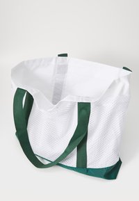 Sac en filet avec un haut blanc et un bas vert. Dispose de deux anses vertes et d'un intérieur spacieux et ouvert en matériau texturé.