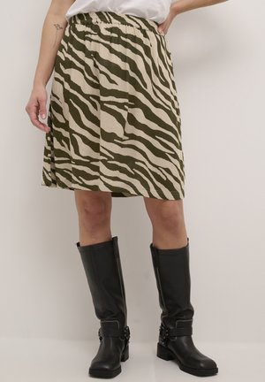 Kvinde iført knælange nederdel med olivengrøn og beige zebra-print, hvid top og sorte knælange læderstøvler med spældetaljer.