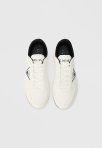 Weiße Sportschuhe mit schwarzen Akzenten. Merkmale sind flache Schnürsenkel, eine strukturierte Zehenkappe, ein Logo-Plättchen und ein gepolsterter Kragen.