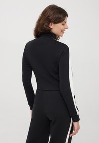 Czarna, krótka bluza z wysokim kołnierzem, z białymi paskami po bokach. Wykonana z miękkiego materiału o gładkiej fakturze i dopasowanym kroju.