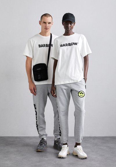 Białe t-shirty z logo "BARROW", szare dresy z bocznymi paskami i naszywką uśmiechu, czarna torba na ramię i sneakersy w szaro-białym kolorze.