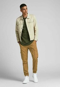 Light beige denim jacket, olive green t-shirt, tan cargo pants with pockets, white high-top sneakers. Simple and functional streetwear design.