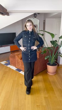 Denim skjortekjole i mørk blå med frontlommer, knapper og kontrastsøm, kombinert med svarte vide bukser og platåstøvler.